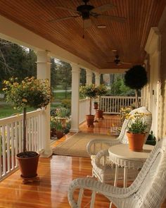 a porch with wicker chairs and potted plants on the front porch, along with a ceiling fan