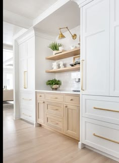 a kitchen with white cabinets and gold handles on the shelves, along with wooden flooring