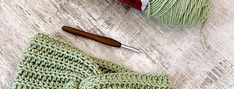 a green knitted bow tie sitting on top of a wooden floor next to yarn and a crochet hook