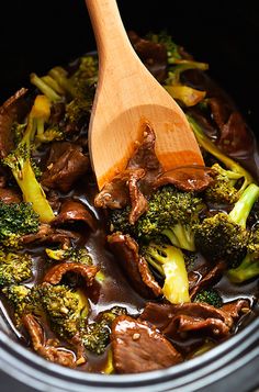 broccoli and mushrooms are being cooked in the crock pot with a wooden spoon