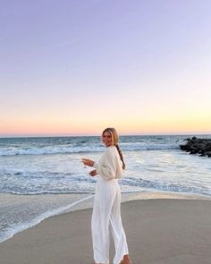 a woman standing on top of a beach next to the ocean holding a cell phone