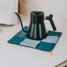 a black teapot sitting on top of a blue towel next to an open book