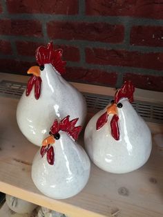 three white vases with red and orange rooster heads sitting on top of a shelf