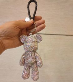 a hand holding a keychain with a teddy bear on it's side