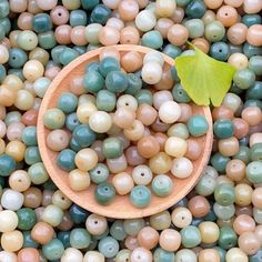 a wooden spoon sitting on top of a pile of green and beige beads with a leaf