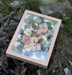 an image of flowers in a frame on the ground with grass and rocks behind it