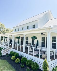 a white house with porches and chairs on the front lawn, surrounded by shrubs