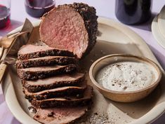 a white plate topped with sliced meat next to a bowl of dip