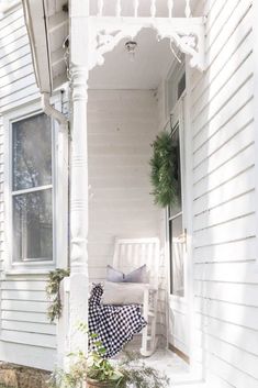 a white porch with a chair and potted plants on the front steps, next to a window