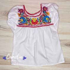 Cute Girl Mexican Puebla blouse made of 100% Cotton poplin fabric. Embroidered frontal detail in silk thread. Shop our entire Puebla Collection here. AGE SHOULDER TO SHOULDER BUST 1 9" 20" 2 10" 21" 4 11" 24" 6 12" 26" 8 13" 28" 10 14" 30" 12 15" 32" 14 16" 34" Measurements are approximate sizes. Lengths may vary by 1-2 inches. CARE:• Cold wash, delicate, inside out. • Hang dry.• Do not machine dry. MADE IN OAXACA, MEXICO Each design and color is unique to each blouse as they are made by differe Festive White Top With Embroidered Sleeves, Festive White Blouse With Embroidered Sleeves, Traditional Cotton Tops With Contrast Embroidery, Festive White Blouse With Embroidered Border, Traditional Multicolor Cotton Peasant Top, Traditional Festive Top With Embroidered Hem, Embroidered Multicolor Blouse For Traditional Ceremonies, Traditional Festive Tops With Embroidered Hem, Traditional White Peasant Top With Embroidered Neckline