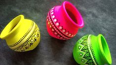 three brightly colored vases sitting on top of a gray surface with designs painted on them