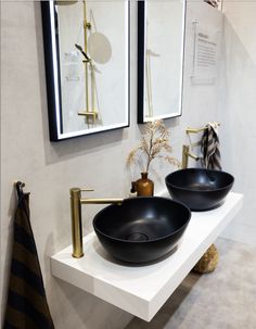 two black bowls are sitting on a white countertop in front of mirrors and gold faucets