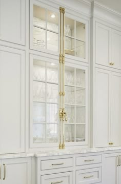 a kitchen with white cabinets and gold trim on the glass front cabinet doors, along with marble counter tops