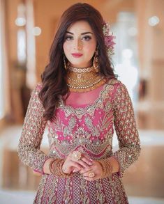 a woman in a pink and gold outfit with jewelry on her neck, standing next to a wall