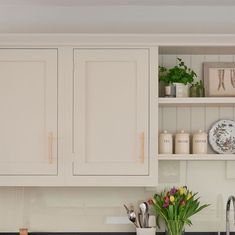 a kitchen with white cabinets and black counter tops, flowers in vases on the sink