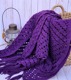 a purple crocheted blanket sitting on top of a table next to a basket