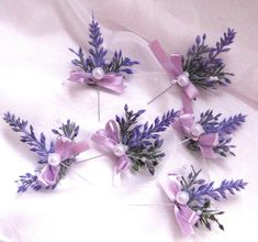 purple flowers and pearls are arranged on a white sheet with pink ribbon around the stems