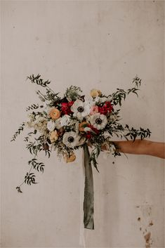 a bridal bouquet being held up by someone's hand in front of a wall