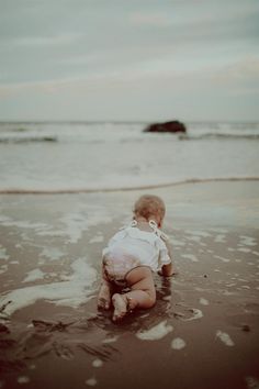 a baby is sitting in the water at the beach and looking out into the ocean