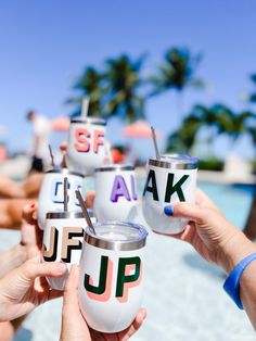 four people holding up cups with the words ask and j f p on them in front of palm trees