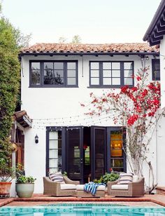 a house with a swimming pool and patio furniture in front of it, surrounded by greenery