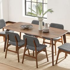 a dining room table with chairs and a vase on the top, in front of a window