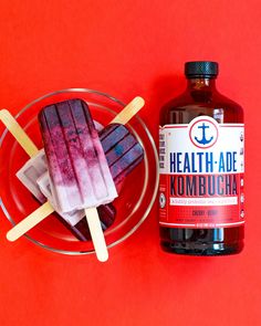 two popsicles and a bottle of kombucha sit on a red surface