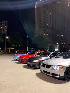 a row of cars parked in front of a tall building with lights on at night