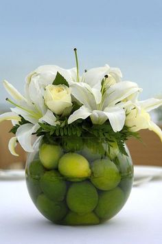 a vase filled with lots of white flowers and green apples on top of a table