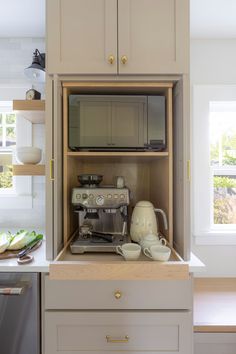 an open cabinet in the middle of a kitchen with coffee maker and other items on it