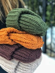 the woman is holding three knitted hats on her shoulders and wearing them in different colors