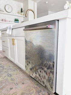 a painting on the side of a refrigerator in a kitchen with white cabinets and an area rug