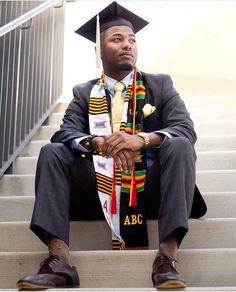 a man wearing a graduation cap and gown sitting on steps with his hands in his pockets