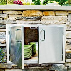 a stainless steel refrigerator sitting next to a stone wall with plates stacked on it's side