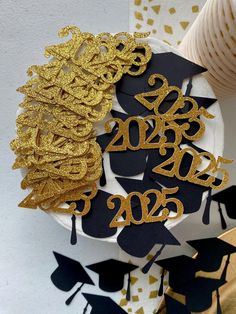 gold and black graduation decorations on top of a white plate with confetti in the background