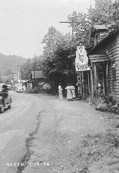 an old black and white photo of people standing on the side of a road next to a building