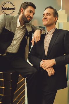 two men sitting next to each other in suits and ties, posing for the camera