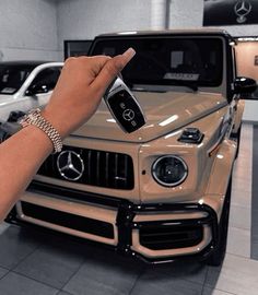 a hand holding a cell phone in front of a mercedes car