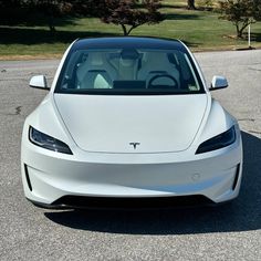 the front end of a white tesla electric car in a parking lot with trees and grass behind it