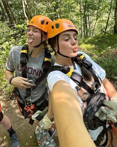 two women in helmets and safety gear taking a selfie while zipping through the woods