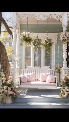 a white porch swing with pink pillows and flowers hanging from it's posts on the front porch