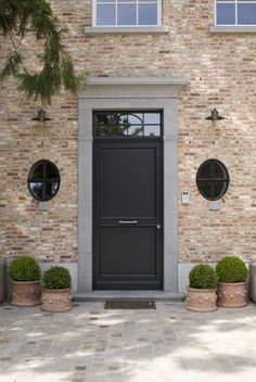 a black front door with round windows and two potted plants in front of it