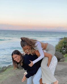 three women hugging each other while standing on the beach near the ocean at sunset or sunrise