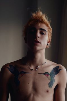 a shirtless man with red hair and tattoos on his chest is looking at the camera