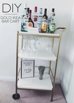 a gold bar cart with liquor bottles and glasses on it, sitting next to a wall