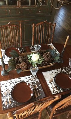 a wooden table with place settings and pine cones on the top, along with candles