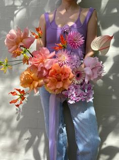 a woman standing next to a wall holding a bouquet of flowers in front of her