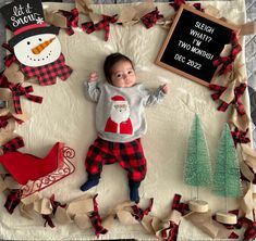 a baby laying on top of a blanket next to christmas decorations and a chalkboard