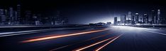 the city skyline is lit up at night with long exposure and light streaks on the road