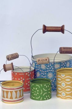 four tins with cork handles and painted designs on them, one has a wine bottle in the top